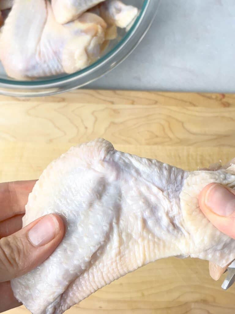 A hand holding a raw chicken wing.
