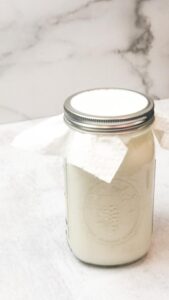 Milk and kefir grains in a glass jar with a paper towel on top and closed with a lid.