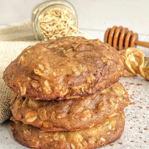 Three Oatmeal Chocolate Chip Cookies with some peanut butter and oatmeal in the background.