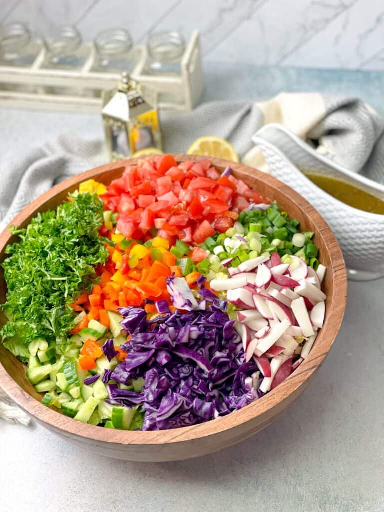 A bowl of chopped tomatoes, colored pepper, cabbage, radish, parsley, and lettuce is ready to pair with the tart savory fattoush dressing for an amazing fattoush bowl.