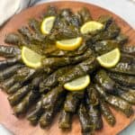 A dish of juicy grape leaves stuffed with rice and veggies and decorated with lemon slices.