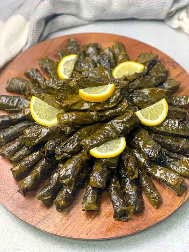 A dish if juicy grape leaves stuffed with rice and veggies and decorated with lemon slices