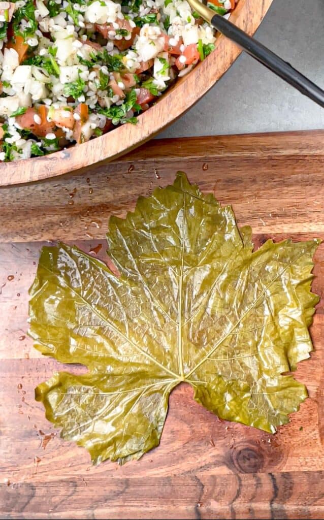 A grape leaf with rough side facing up ready to be filled with veggies and rice