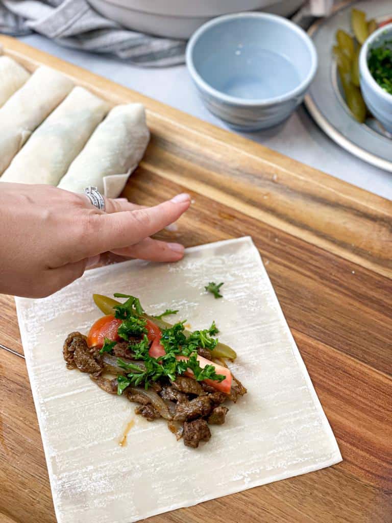 Fold the bottom of the wrapper over the shawarma filling. Then, fold in the sides and roll.