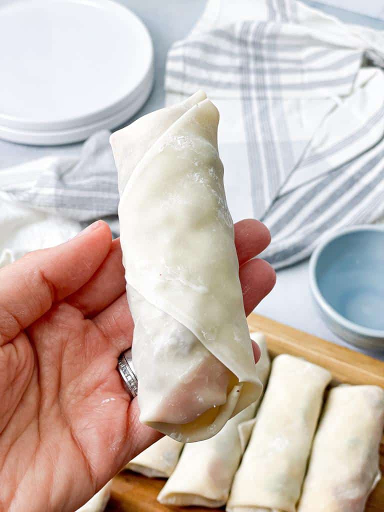 Lightly wet the exposed edge of the spring roll wrapper with your fingertip and continue rolling to seal the egg roll.