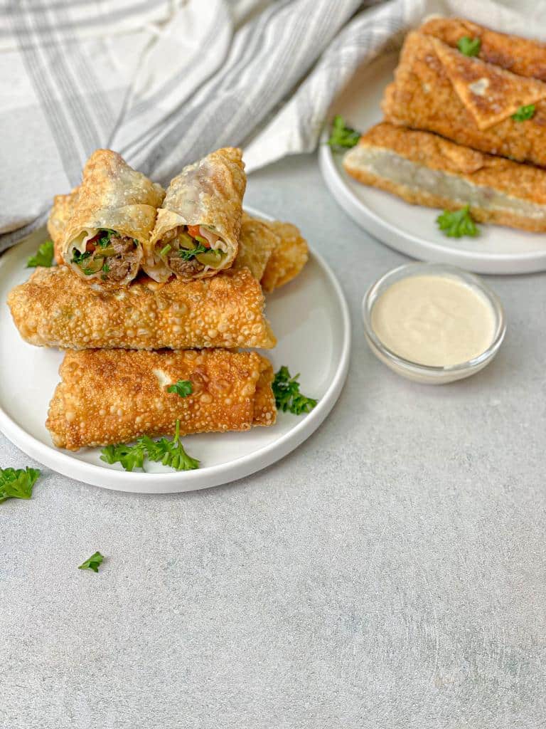A plate of shawarma egg rolls with a small bowl of tahini dip