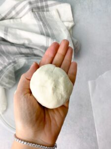 a woman holding a perfect round naan bread dough