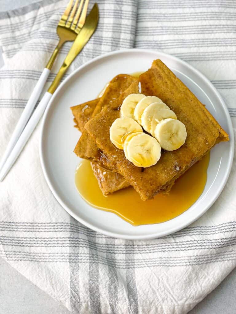 Sheet Pan Pumpkin Pancakes on the white plate topped with syrup and bananas.