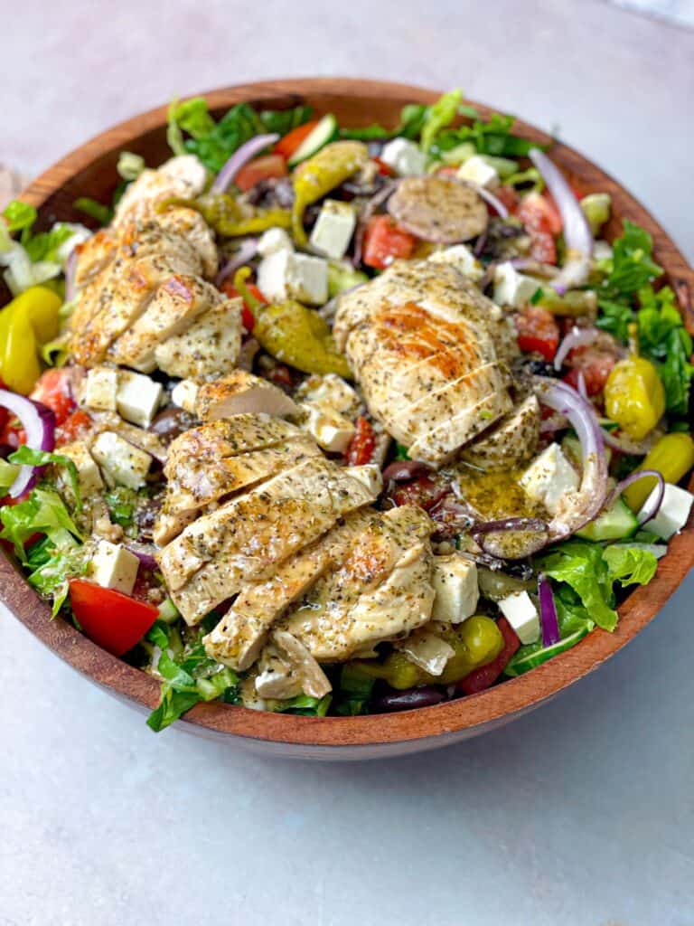A bowl of Greek salad topped with grilled chicken. Pour the Greek dressing and enjoy the taste.