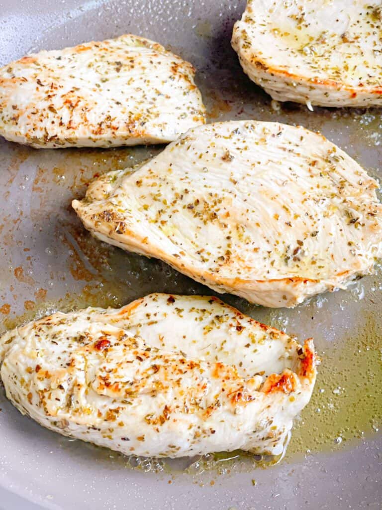 Seared chicken breasts in a pan have a light golden color and juicy texture