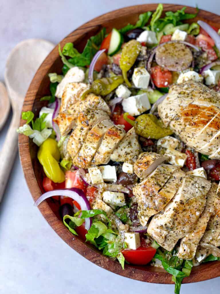 A bowl of healthy salad with Greek dressing and sliced grilled chicken