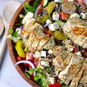 A bowl of healthy salad with Greek dressing and sliced grilled chicken.