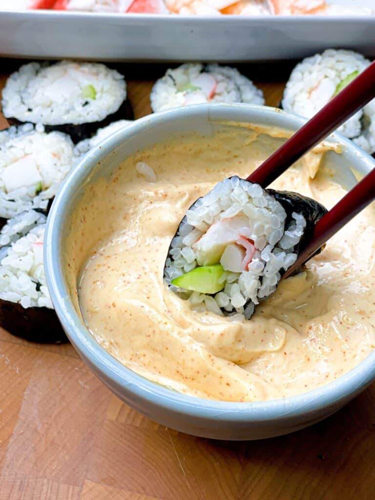 A roll of sushi dipped in a bowl of tangy creamy dipping
