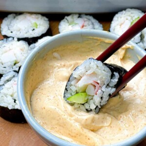 Chopsticks dipping the sushi in spicy mayo sauce.