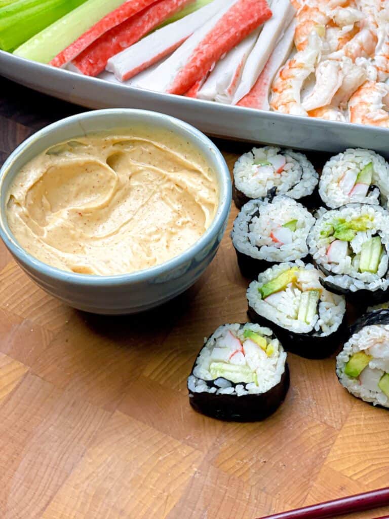 A bowl of homemade mayo sauce for sushi next to sushi rolls and some shrimp