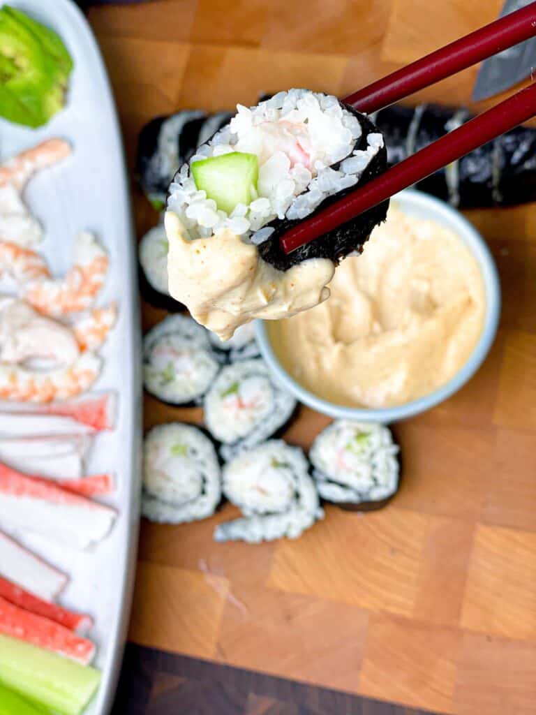 A sushi roll between chopsticks dipped in tangy mayo sauce for sushi