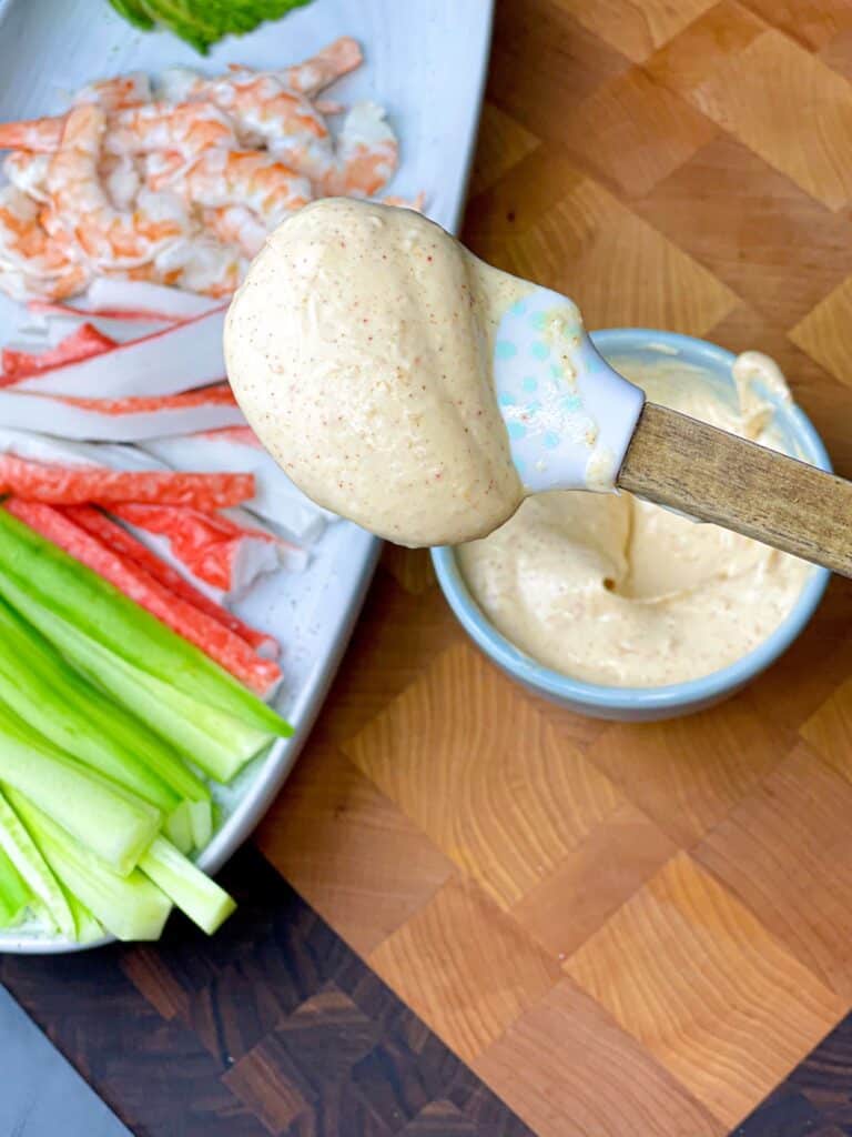 A spoon dipped in tangy mayo sauce with a plate of seafood