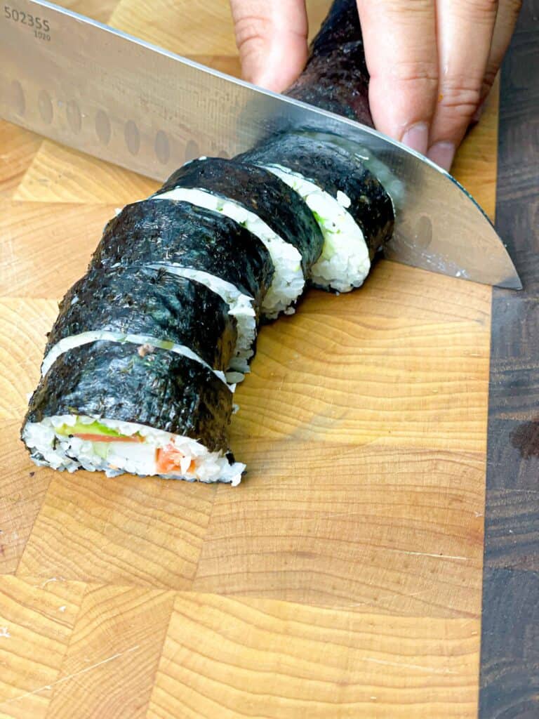 A lady cutting sushi rolls into similar size pieces with a sharp knife