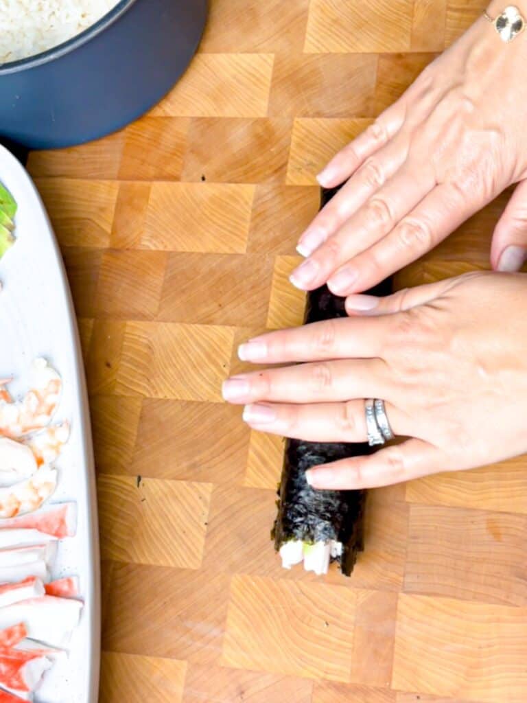 A lady pressing firmly all across the sushi rolls