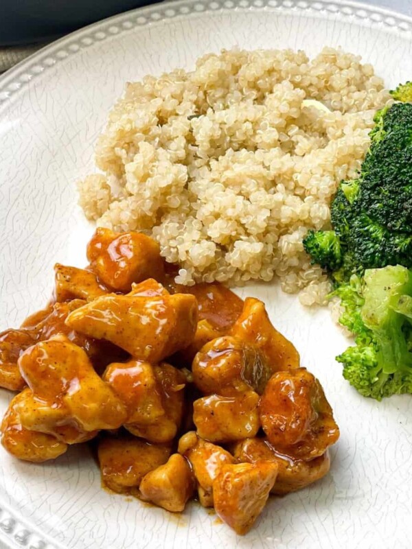 A plate packed with some sticky orange chicken, steamed broccolis, and quinoa.