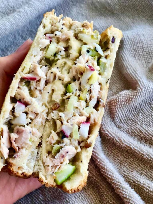 A hand holding a mix of tuna, pickles, radish, gouda cheese and chopped celery sandwiched in toasted bread.