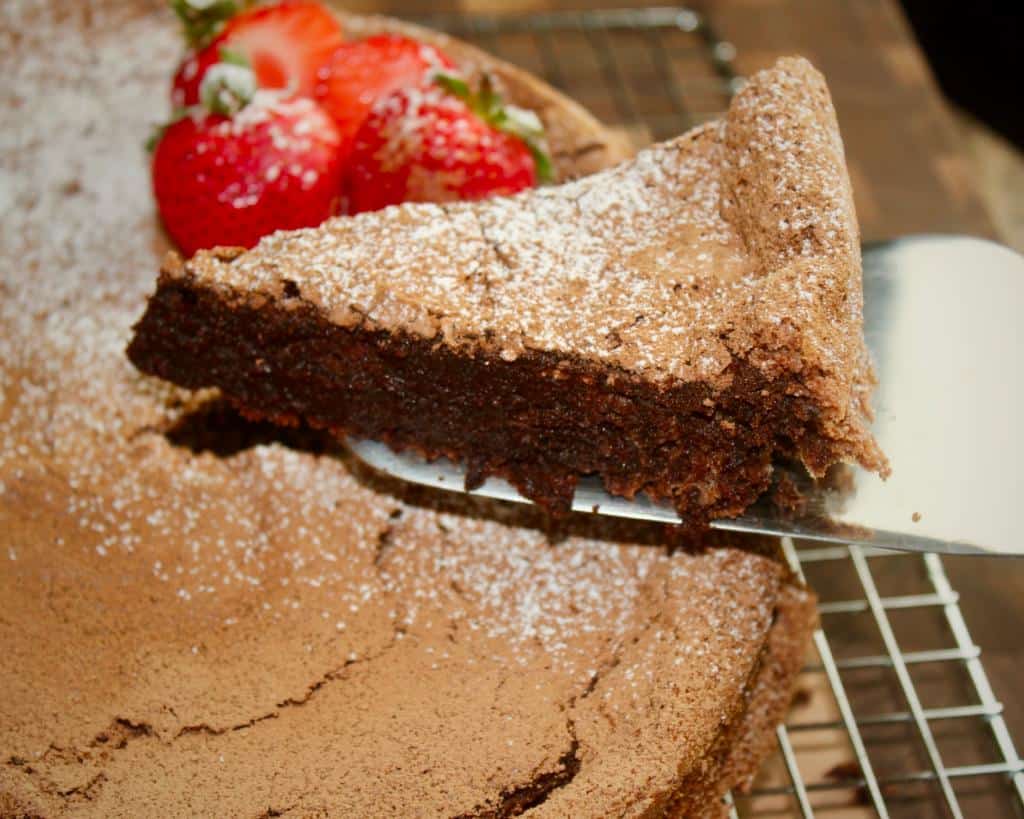 A slice of fudge chocolate cake topped with powdered sugar and some strawberries
