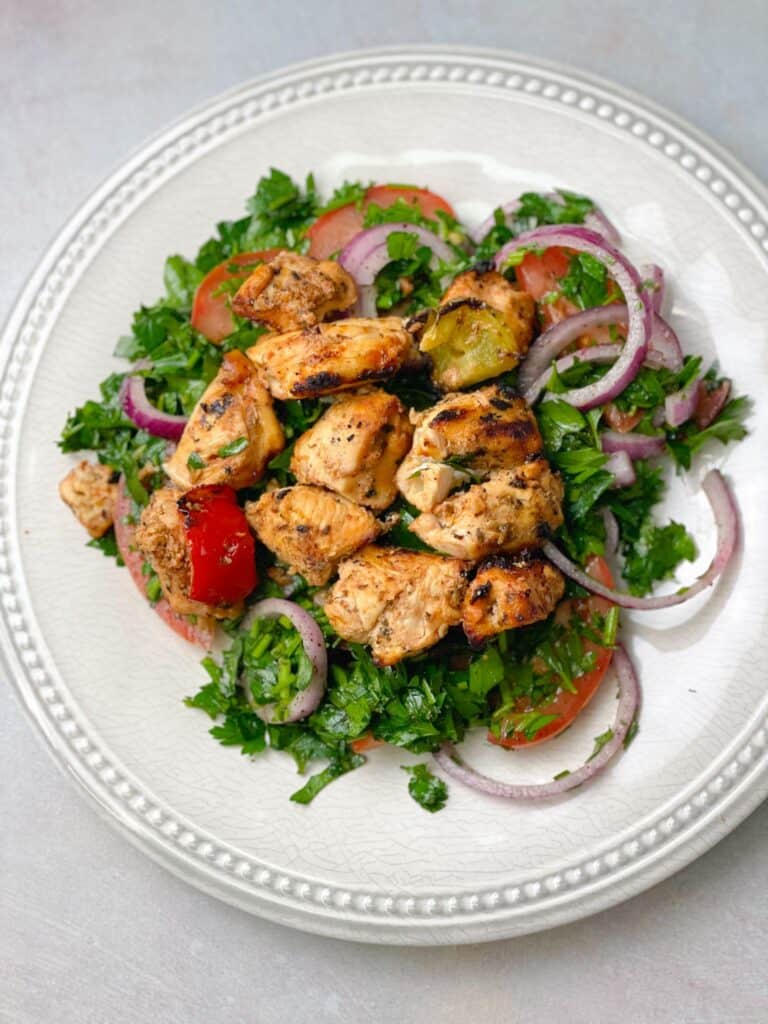a plate of chicken shish tawook served with sumac red onions salad