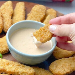 A hand dipping a chicken finger in a dipping sauce.