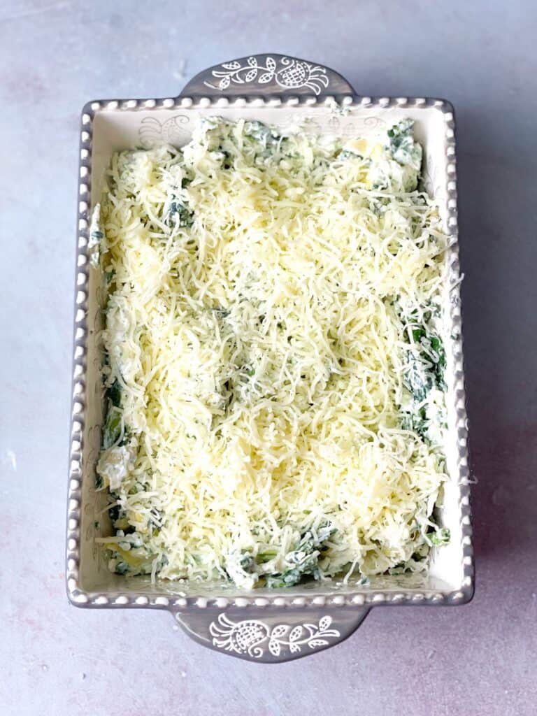 A baking dish with the spinach artichoke mix layered with cheese.