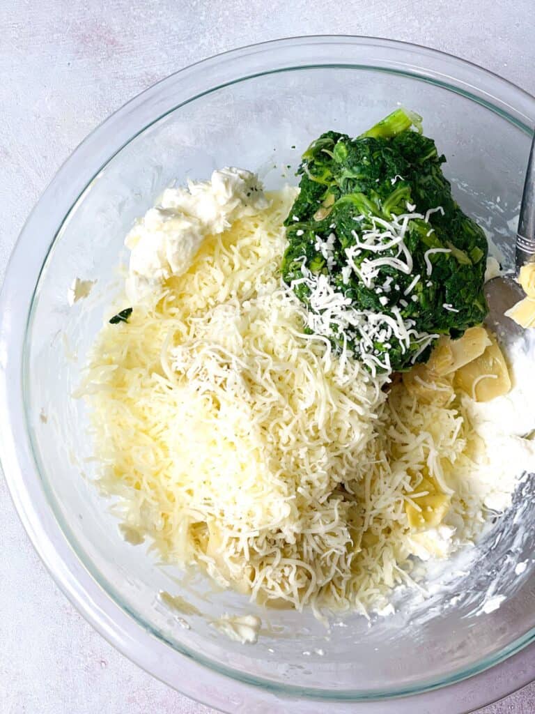 A bowl with a mix of cream cheese, melted butter, frozen spinach, water, half the amount of mozzarella cheese, little salt, and black pepper.
