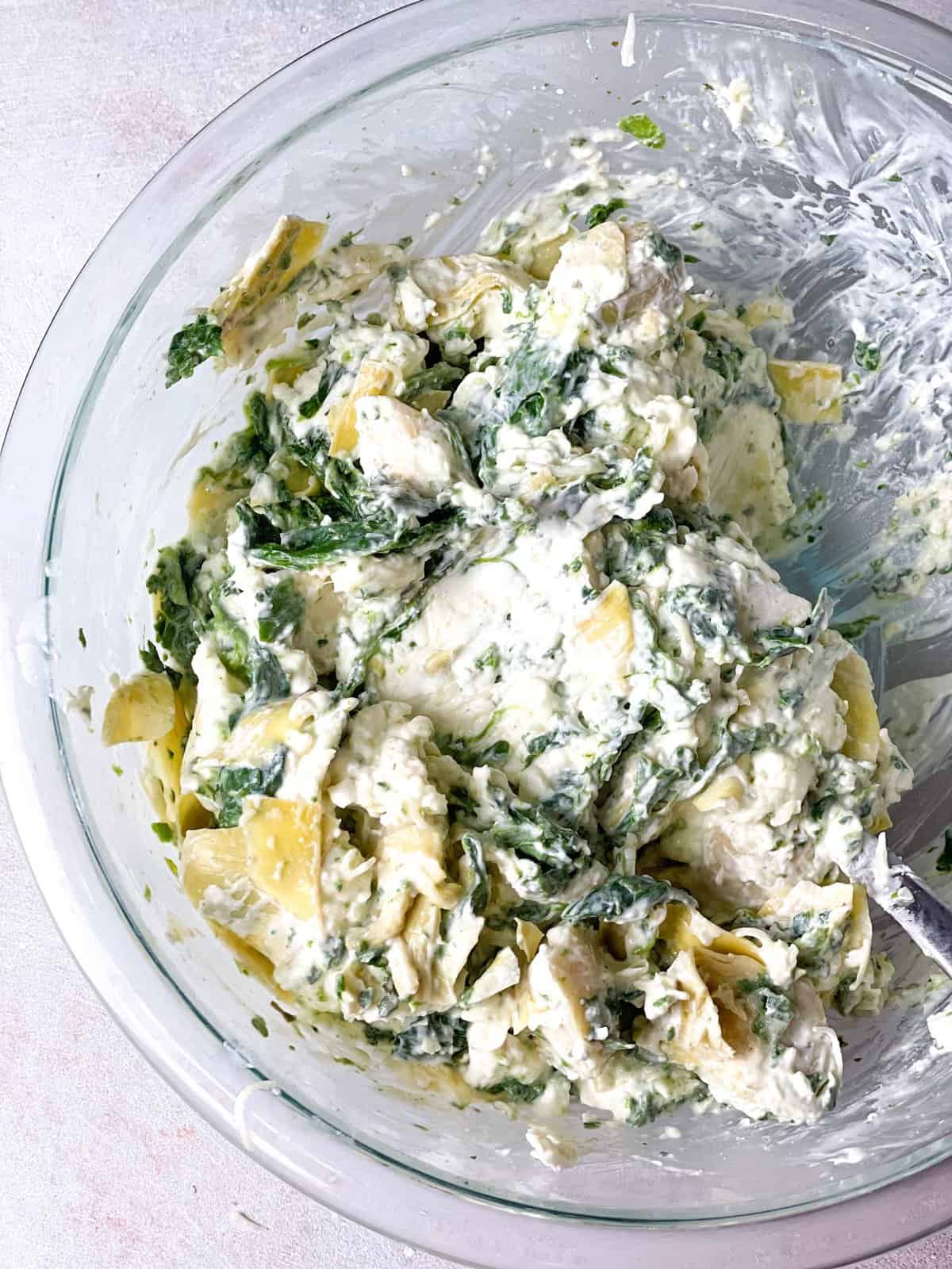 A bowl with the marinated artichoke hearts mixed with cream cheese, butter, spinach, water, mozzarella cheese, and seasoning.