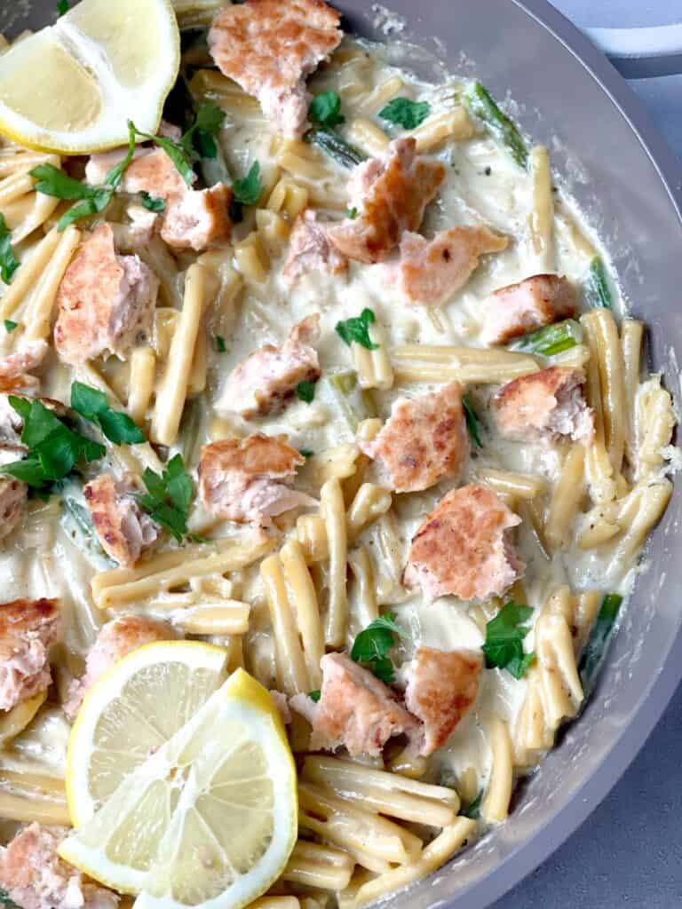 Some salmon flakes mixed with creamy pasta garnished with chopped parsley and lemon wedges is a luscious meal for dinner