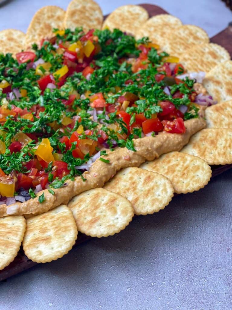 Hummus topped with fresh veggies like onions, tomatoes, and parsley is a perfect dip especially for crackers.