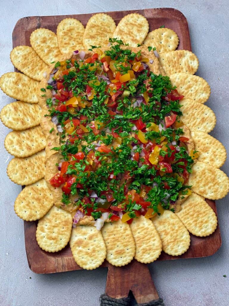 Layered hummus dip topped with veggies with some crackers to dip in