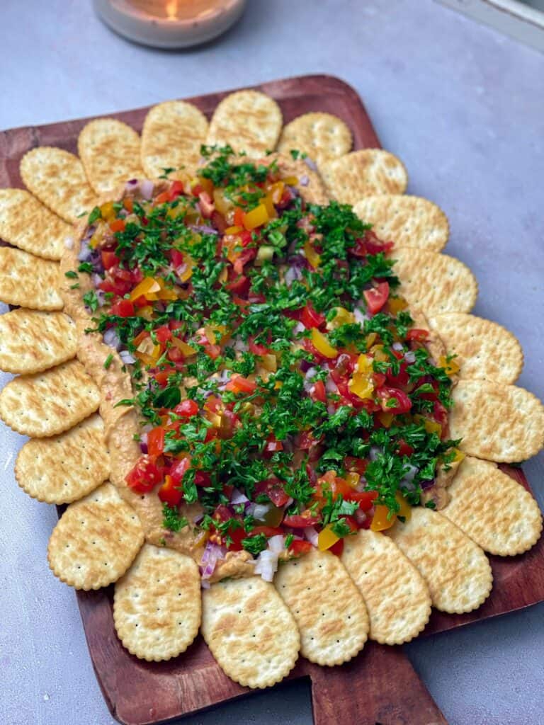 A beautiful platter of hummus dip and bright veggies with crunchy crackers for a satisfying meal
