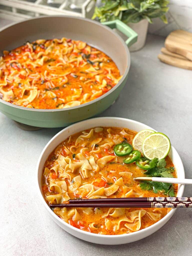 A bowl and a casserole of the hearty Thai Red Curry Noodle Soup which is rich in bold flavors and fresh ingredients.