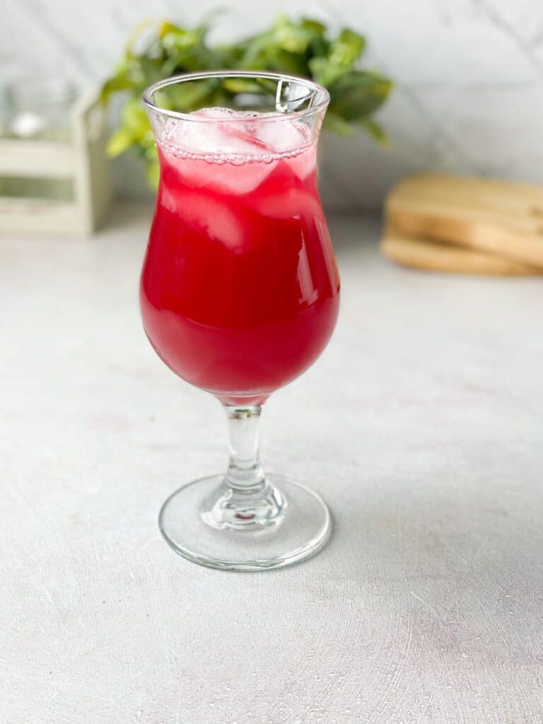 A tall glass of bright red homemade cranberry juice with a few ice cubes. 