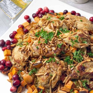 Juicy chicken thighs are marinated in a sauce and served over a bed of fluffy rice with hearty veggies garnished with toasted almonds and fresh cranberries