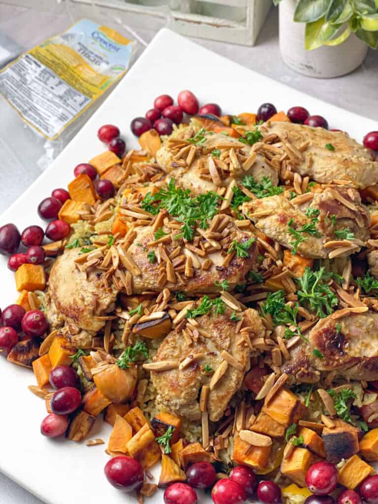 Juicy chicken thighs are marinated in a sauce and served over a bed of fluffy rice with hearty veggies garnished with toasted almonds and fresh cranberries