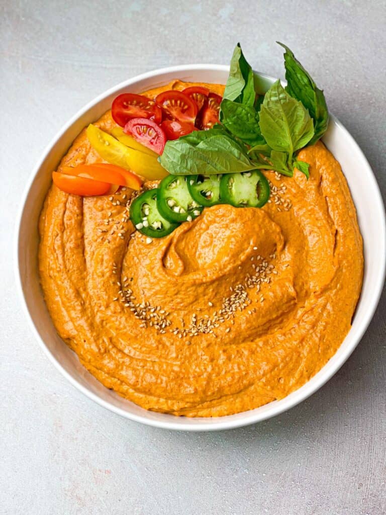 Spicy roasted red pepper hummus garnished with peppers, mint leaves , and jalapeno peppers with some roasted sesame seeds on top.