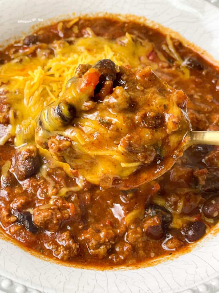 thick and hearty chili with melted cheddar cheese served and being eaten with a spoon