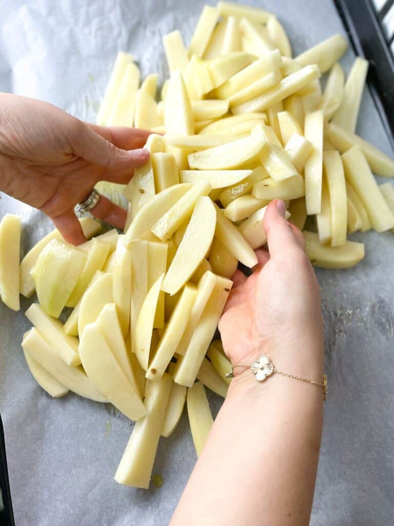 a woman mixing the French fries with salt and olive oil
