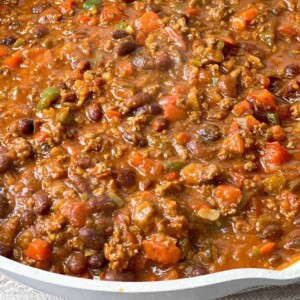 thick hearty chili made with ground meat, onion, colored peppers, tomatoes, and beans with a group of peppers