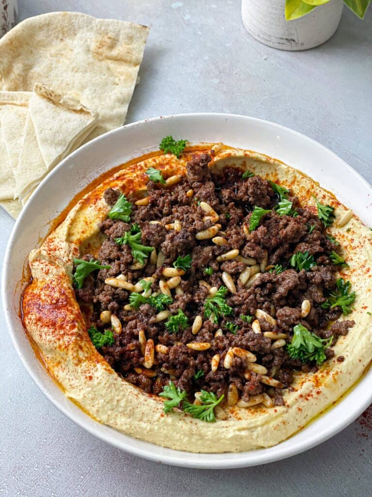 hummus sprinkled with paprika topped with ground meat, pine nuts, and fresh parsley