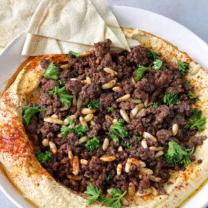 A plate of hummus topped with well seasoned ground meat with fried pine nuts and chopped parsley