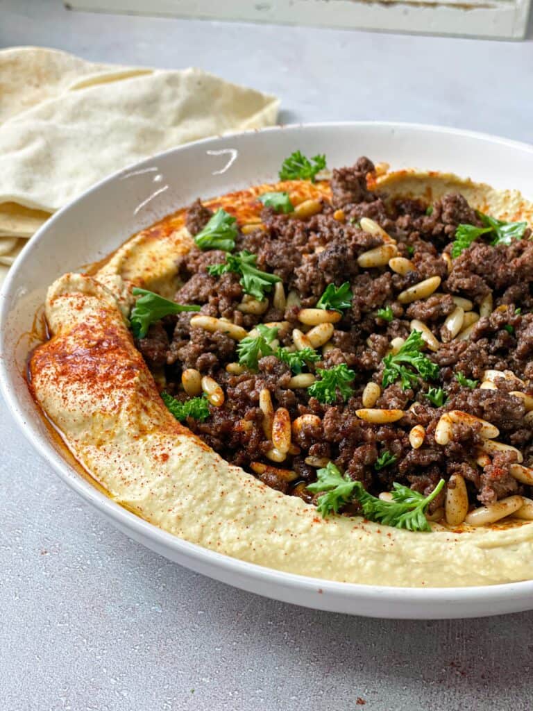 hummus with seasoned ground meat, pine nuts, and fresh herbs drizzled with olive oil and served with pita bread