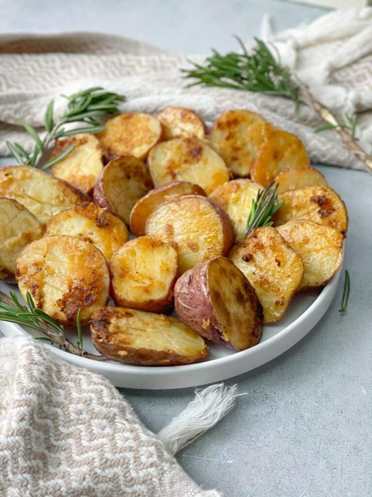 baby potatoes are cut into halves and baked in the oven with olive oil, garlic, rosemary, and parmesan served on a plate and decorated with rosemary sticks