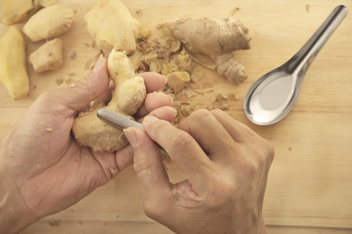 a hand peeling a ginger root with a silver spoon