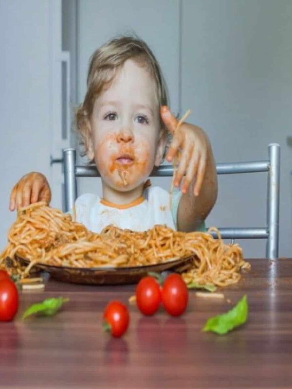 A little child is eating spaghetti made with a vegan sauce. The child has red spots of the sauce all over his mouth.