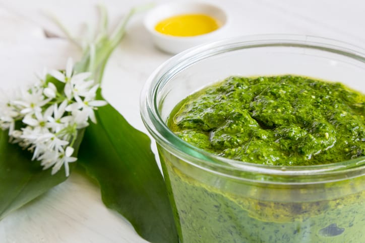 A sauce of avocado, cilantro, mint, and pistachios  ground into cream is in a glass jar on a table.
